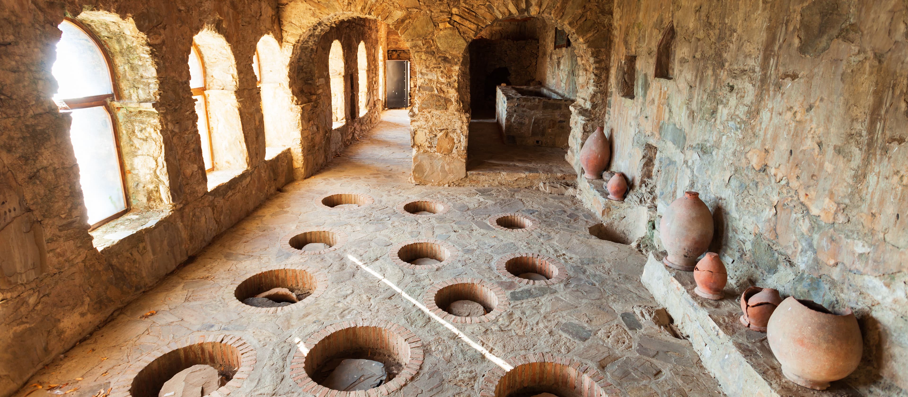 Nekresi Monastery Qvevri Cellar - Traditional Georgian Winemaking Traditional Georgian winemaker working with qvevri clay vessels in ancient wine cellar with stone walls and wooden tools